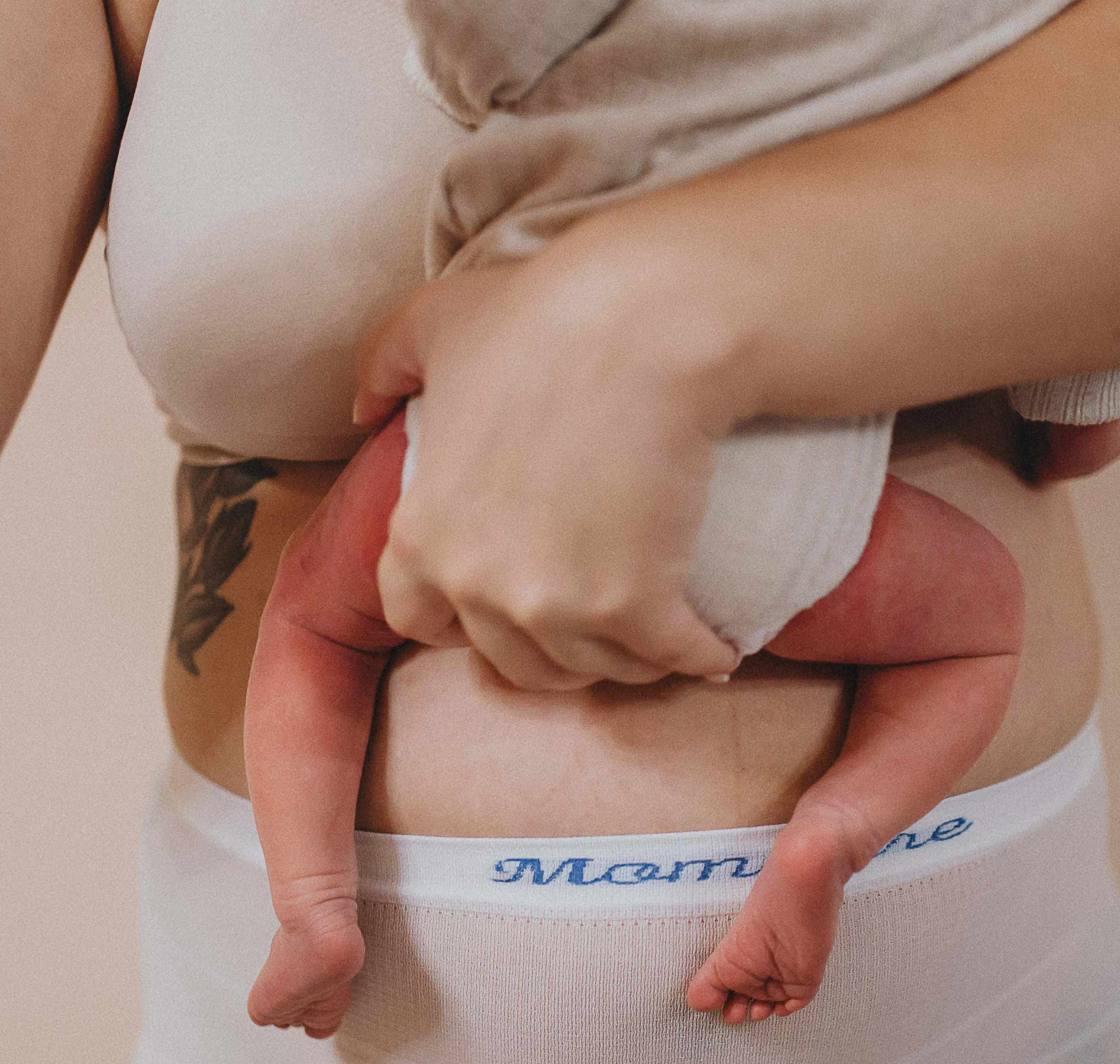 Maminka v MomCare Poporodních kalhotkách držící své novorozené dítě